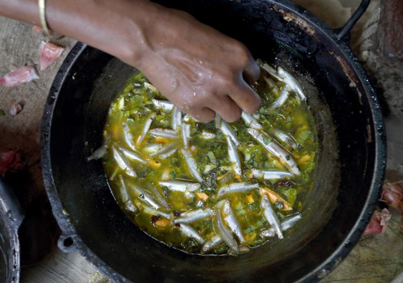 A woman cooking mola and orange sweet potato curry in her kitchen in Jessore, Bangladesh.